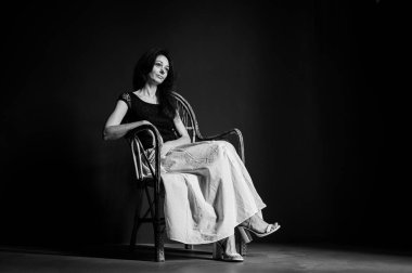 Heyecanlı, neşeli, çılgın, harika duygusal güzel bir kızın portresi ahşap hasır koltukta, karanlık arka planda izole bir şekilde oturuyor.