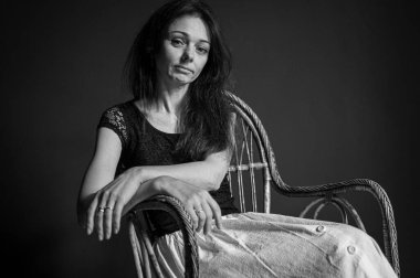 Heyecanlı, neşeli, çılgın, harika duygusal güzel bir kızın portresi ahşap hasır koltukta, karanlık arka planda izole bir şekilde oturuyor.