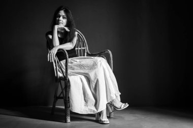 Heyecanlı, neşeli, çılgın, harika duygusal güzel bir kızın portresi ahşap hasır koltukta, karanlık arka planda izole bir şekilde oturuyor.