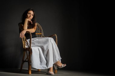 Heyecanlı, neşeli, çılgın, harika duygusal güzel bir kızın portresi ahşap hasır koltukta, karanlık arka planda izole bir şekilde oturuyor.