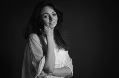 Siyah beyaz klasik fotoğraf. Şüpheci ve şüpheli duygularla gülümseyen duygusal genç kız, düşünceli ve dalgın. Gri arka planda alaycı bir kadının portresi. Seçici odak