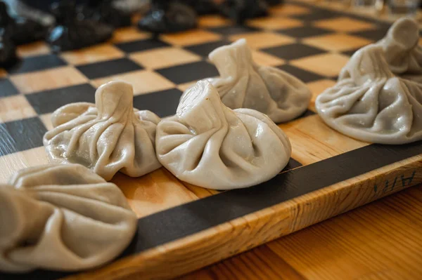 Traditional Georgian dish, khinkali Kalakuri, on wooden table, chess board, rustic, side view, black and light dough, chess game. Selective focus, side view. Meat and cheese dishes