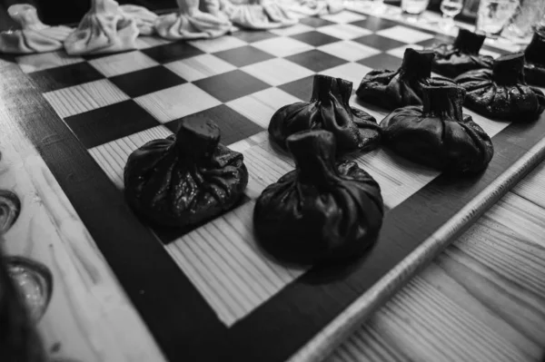 黑白经典照片近视 传统的格鲁吉亚菜 Khinkali Kalakuri 放在木制桌子上 棋盘上 黑面和面团 象棋游戏 有选择的重点 侧面观点 — 图库照片