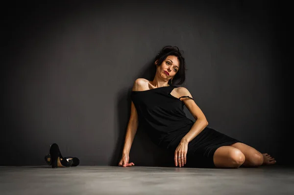 灰色の背景に床に座って黒のドレスで疲れ 若い美しい官能的な女性のスタジオの肖像画 うつ病疲労孤独思慮深さ — ストック写真