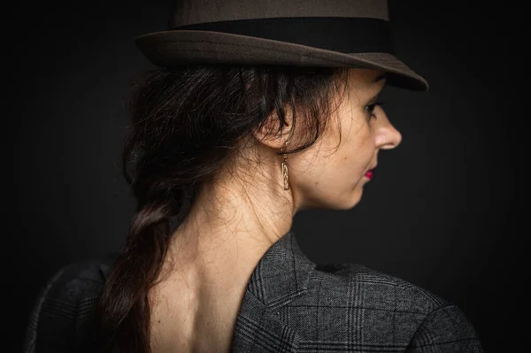Close-up portrait of an elegant, beautiful, sexy woman in a gray suit, wearing a man\'s hat, rear view from the back