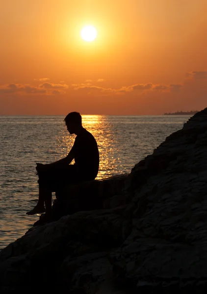 Человек, сидящий на камне и наслаждающийся закатом — стоковое фото