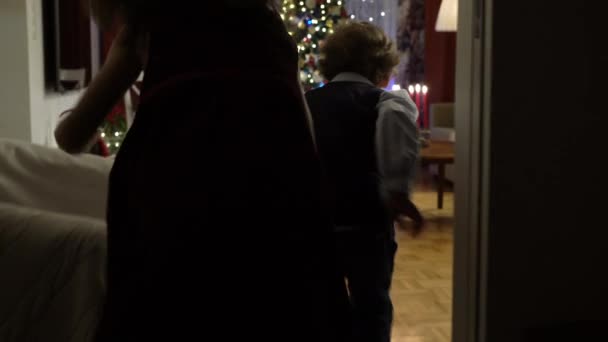 Kleine jongen en meisje rennen naar cadeautjes onder de kerstboom — Stockvideo