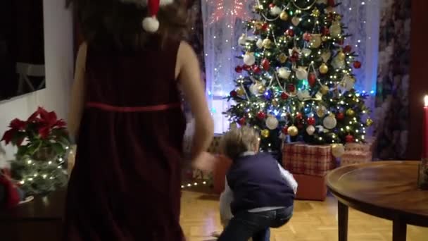 Mały chłopiec i dziewczyna biegnie do prezentów pod choinką — Wideo stockowe