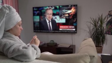 Genç bir kadın manikür yapıyor. Oturma odasında, elinde televizyonla oturuyor.