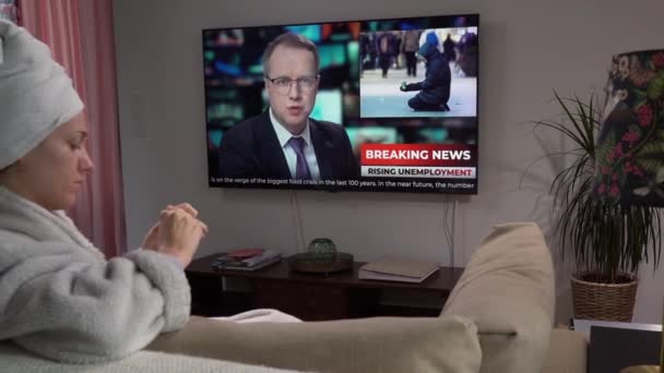 Молодая женщина сидит на диване в гостиной с телевизором — стоковое видео