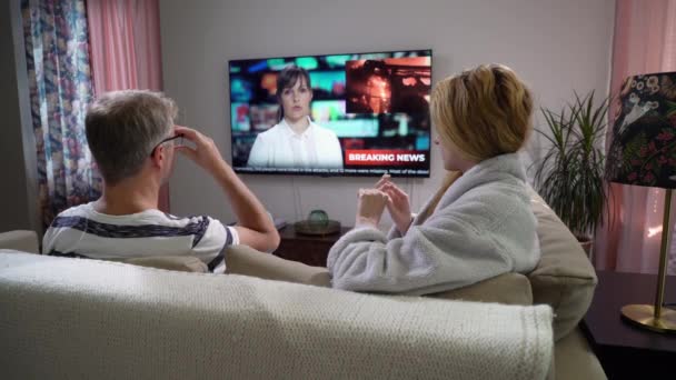Οικογενειακό ζευγάρι Βλέποντας ειδήσεις τηλεόραση κάθεται στον καναπέ στο σαλόνι — Αρχείο Βίντεο