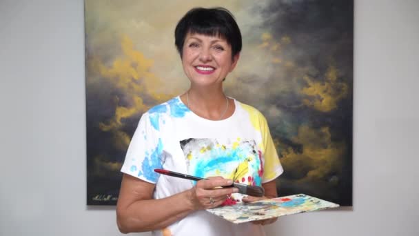 A mature female artist poses against the background of her painting — Stock Video