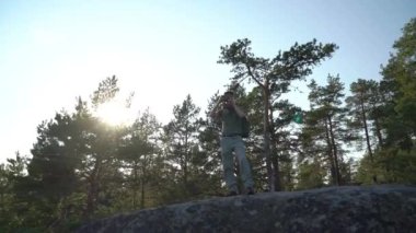 Finlandiya 'da dağ ormanlarında yürüyüş ekipmanlarıyla gezen olgun bir adam ve eski model bir kamerayla nefes kesici kuzey manzaralarını fotoğraflıyor.
