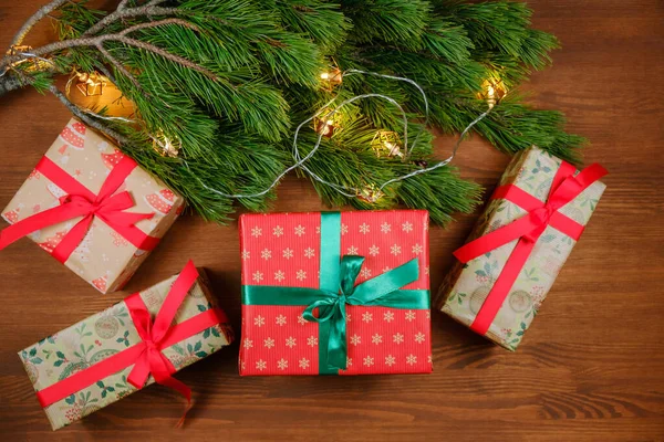 Noel hediyeleri ahşap bir masada Noel ağacı ve yılbaşı ışıkları dallarıyla
