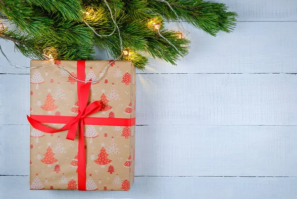 Noel ağacı dalları ve ışıkları olan beyaz ahşap arka planda noel hediyesi kutusu. Xmas ve Mutlu Yıllar teması. Düz yerde, üst tarafta. Boşluğu kopyala