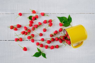 Beyaz ahşap arka planda sarı fincanda olgun taze ahududular. Üst görünüm