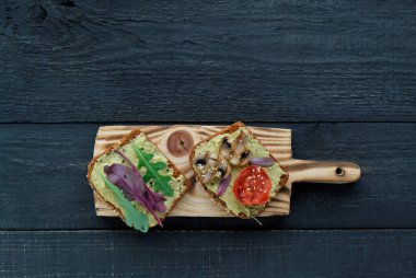 Izgara domatesli avokado tostu, ızgara mantar ve koyu ahşap masada salata. Sağlıklı yiyecekler ve vejetaryen diyet kavramları