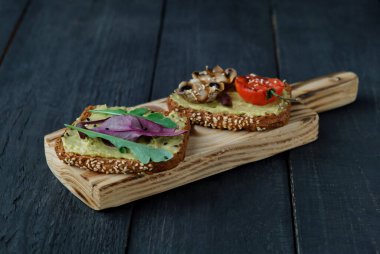 Izgara domatesli avokado tostu, ızgara mantar ve koyu ahşap masada salata. Sağlıklı yiyecekler ve vejetaryen diyet kavramları