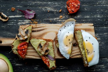 Izgara domatesli avokado tostu, ızgara mantar ve koyu ahşap masada kızarmış yumurta. Manzarayı kapat. Üst Manzara. Sağlıklı yiyecekler ve vejetaryen diyet kavramları
