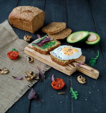 Izgara domatesli avokado tostu, ızgara mantar, salata ve koyu ahşap masada kızarmış yumurta. Sağlıklı yiyecekler ve vejetaryen diyet kavramları