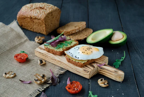 鳄梨吐司与烤西红柿 烤蘑菇和煎蛋在切菜板上的深色木桌 健康食品和素食概念 — 图库照片