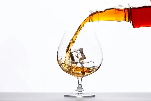 Pouring whiskey drink into a glass with ice cubes on white background