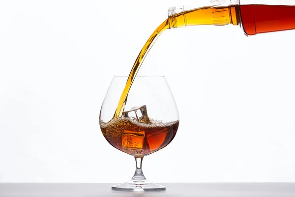 Pouring whiskey drink into a glass with ice cubes on white background