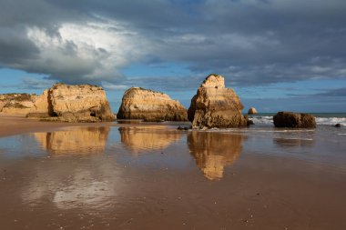 Portekiz, Portimao 'daki Praia dos Tres Castelosn. Kireçtaşı kayaları ve bulutlar alçak gelgit suyuna yansıyor