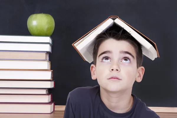 Ung pojke med bok om hans huvud och staplade böcker — Stockfoto