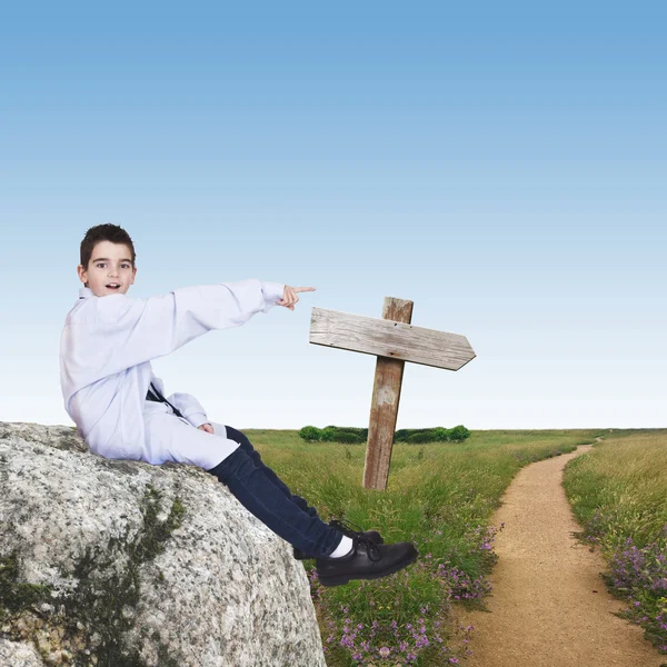 Niño sentado en la piedra que indica la dirección del viaje — Foto de Stock