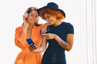 Cep telefonu ve kulaklığı olan kızlar sokakta müzik dinliyorlar.