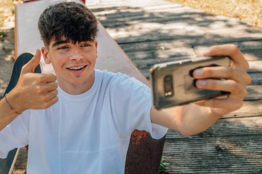 Genç çocuk cep telefonuyla kayıt yapıyor ya da fotoğraf çekiyor.