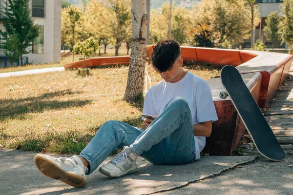 路上で携帯電話とスケートボードを持つ10代の男の子 — ストック写真