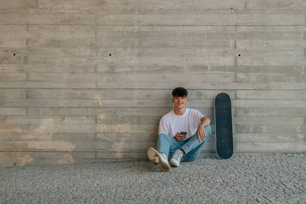 壁に携帯電話とスケートボードを持つ10代の男の子 — ストック写真