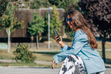 Genç kız çömelmiş, cep telefonuyla çömelmiş.