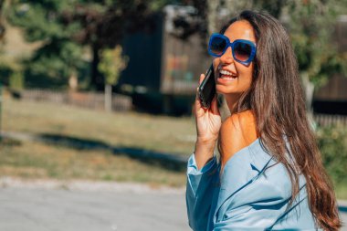 Dışarıda cep telefonu ve güneş gözlüklü bir kızın portresi.