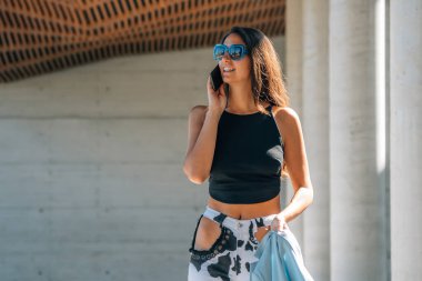 Gün batımında kız sokakta cep telefonuyla konuşuyor.