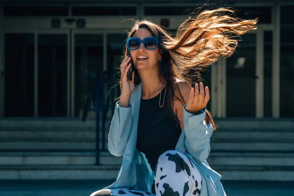 Uzun Saçlı Güneş Gözlüklü Bir Kadın Cep Telefonuyla Arka Planda — Stok fotoğraf