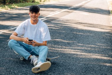 Kaykaylı ve kulaklıklı çocuk yolda.