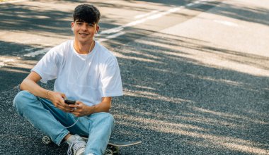 Cep telefonu olan genç bir çocuk yerde oturuyor.