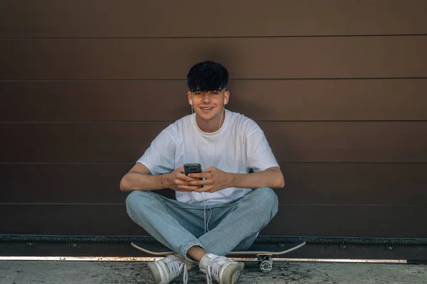 少年坐在滑板上 拿着手机 — 图库照片