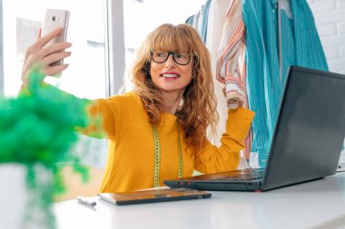Dikiş ve moda atölyesinde cep telefonu kullanan orta yaşlı bir kadın