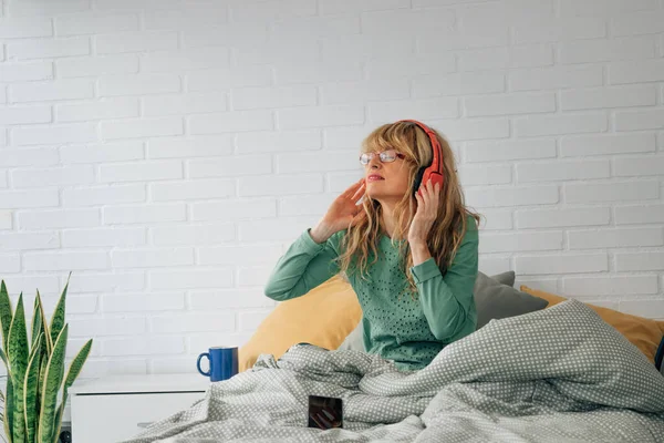 ベッドで音楽を聴くヘッドフォンを装着した家の女性 — ストック写真