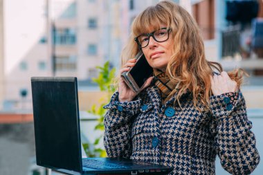 Sokakta cep telefonu ve bilgisayarı olan kadın.