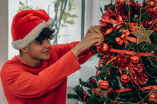 十代の男の子飾るクリスマスツリーとともにサンタクラスの帽子 — ストック写真