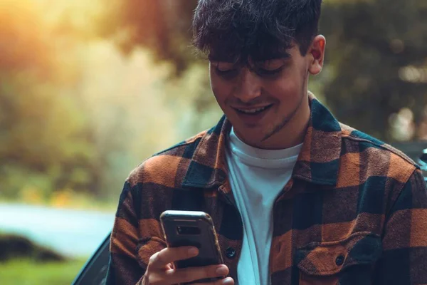 Glimlachende Jonge Man Zoek Naar Mobiele Telefoon Buiten Herfst Setting — Stockfoto