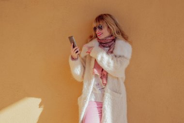 Kadın cep telefonuyla sokak duvarına yaslanıyor.