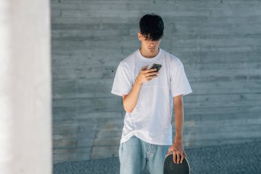 Sokakta cep telefonu ve kaykayı olan genç bir adam.