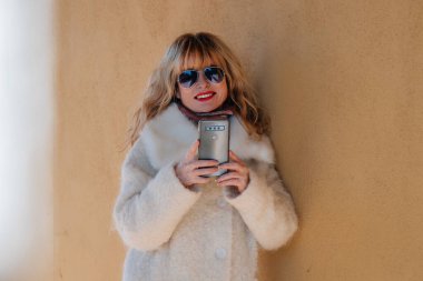 Sokakta ceketli ve cep telefonlu orta yaşlı bir kadın.