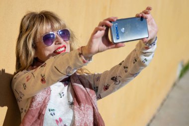 Sokakta cep telefonlu bir kadın selfie ya da fotoğraf çekiyor.